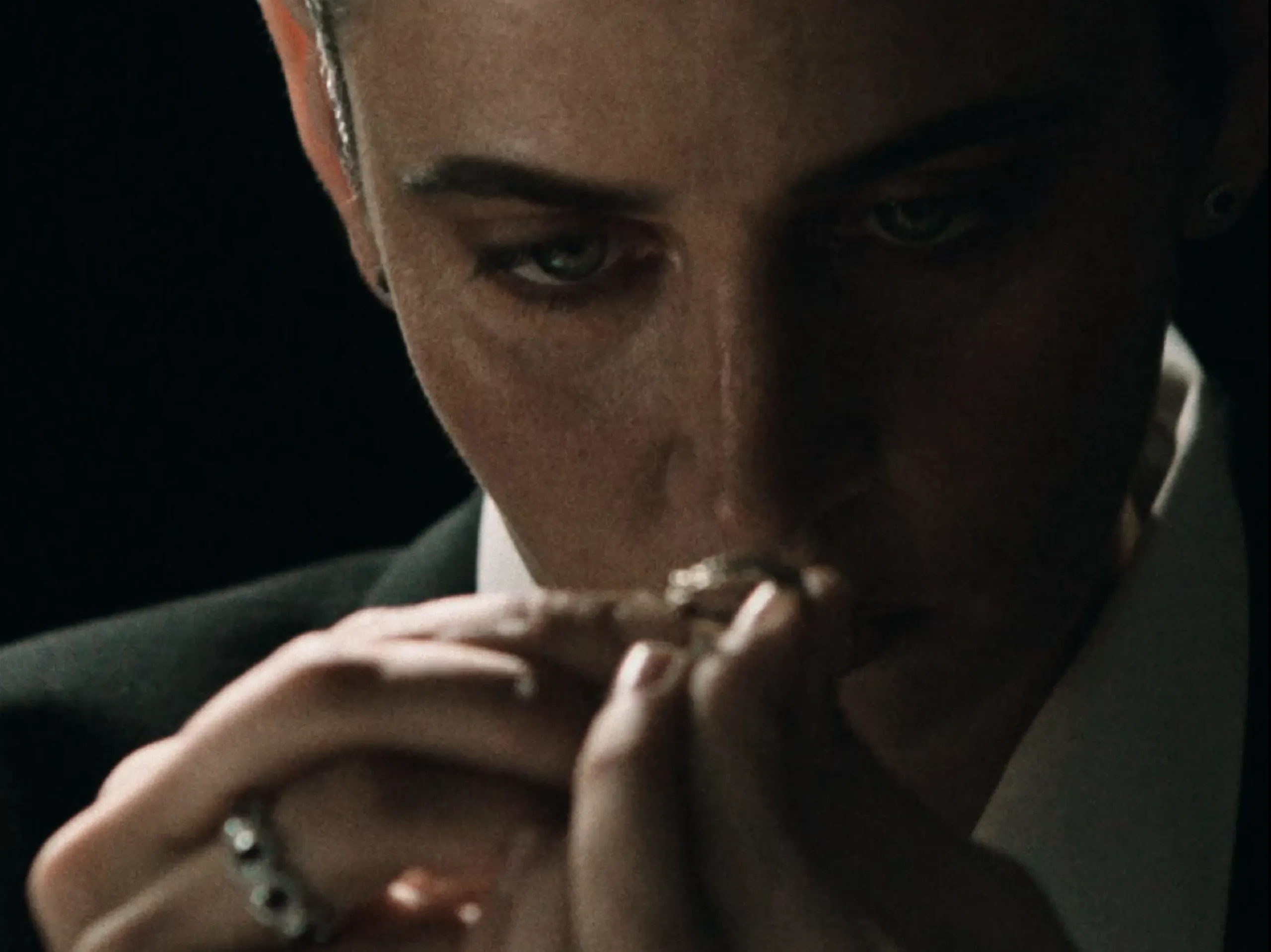 Nina Ornatkiewicz holding a ring close to her face, examining it in low studio light