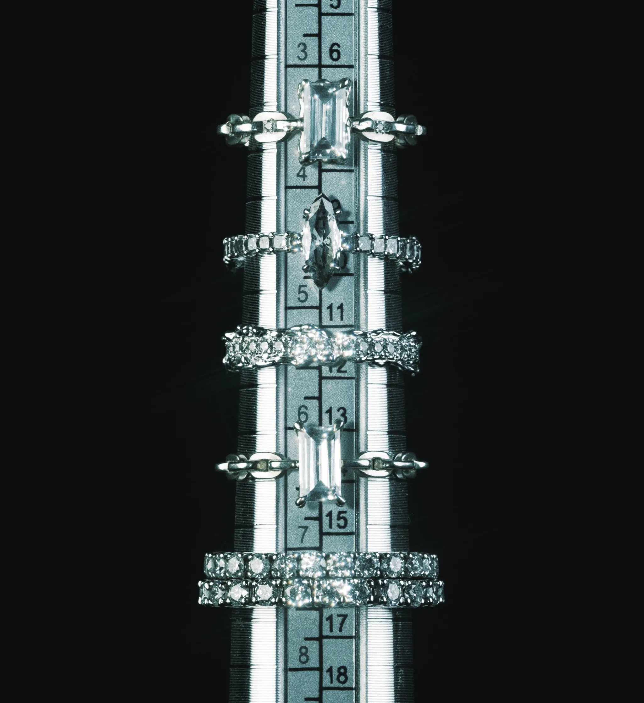 White gold rings set with marquise-cut and square-cut diamonds, arranged along a steel ring sizer against a dark background