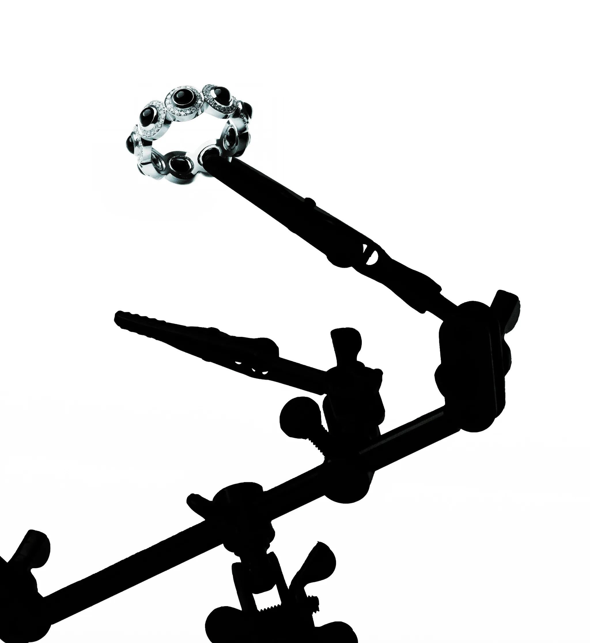 Jeweller's tweezers holding a white gold ring set with black onyx and pavé diamonds, silhouetted against white